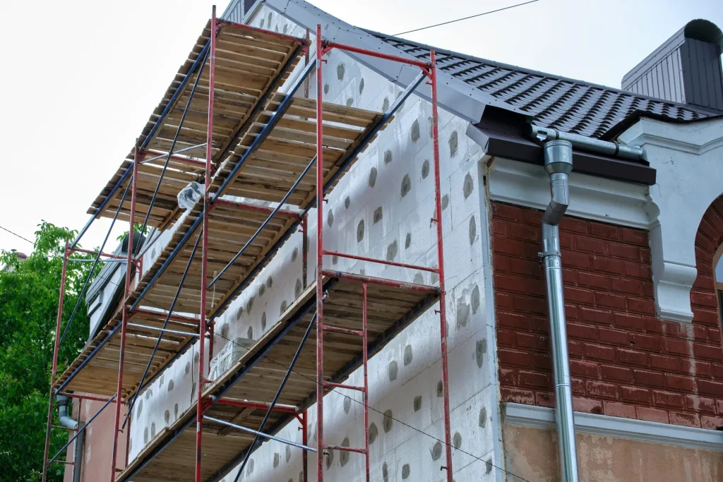 Building facade under renovation works with construction scaffolding frame. Wall insulation with