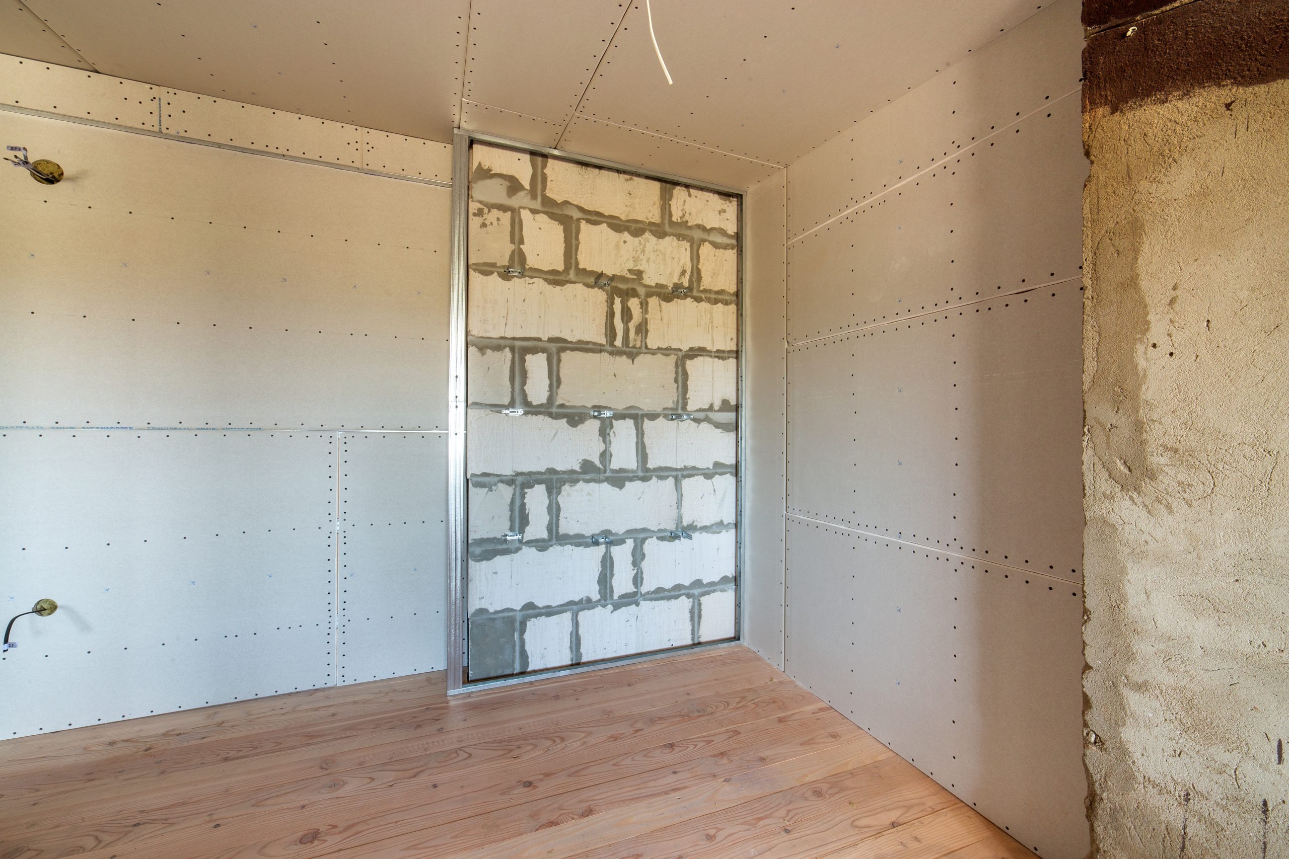 Unfinished brick wall in a room under construction prepared for drywall plates frame installation.